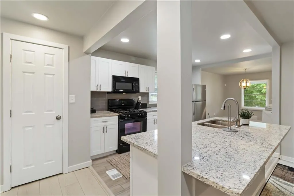 Kitchen with black appliances, light stone counters, recessed lighting, an island with sink, and backsplash