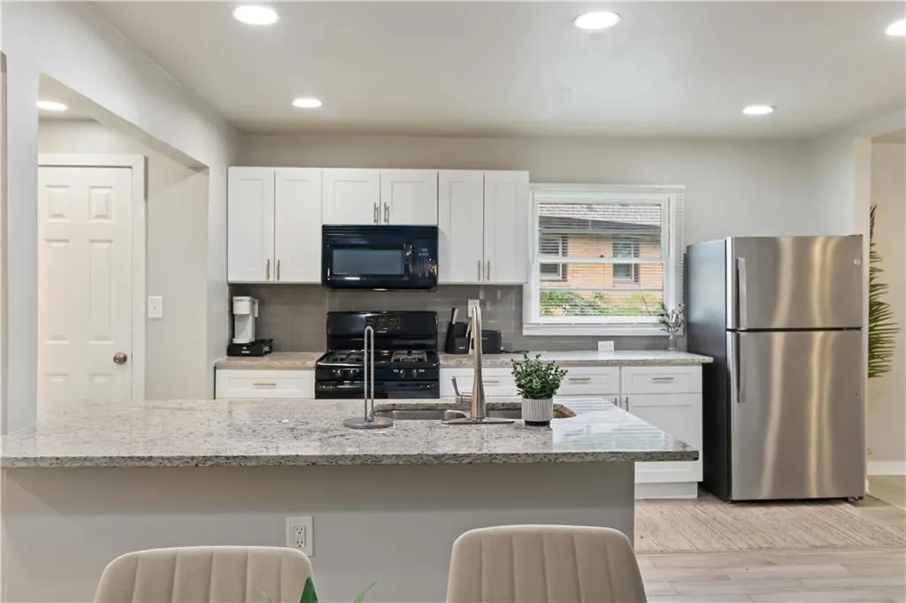 Kitchen featuring white cabinets, black appliances, backsplash, light stone counters, and recessed lighting