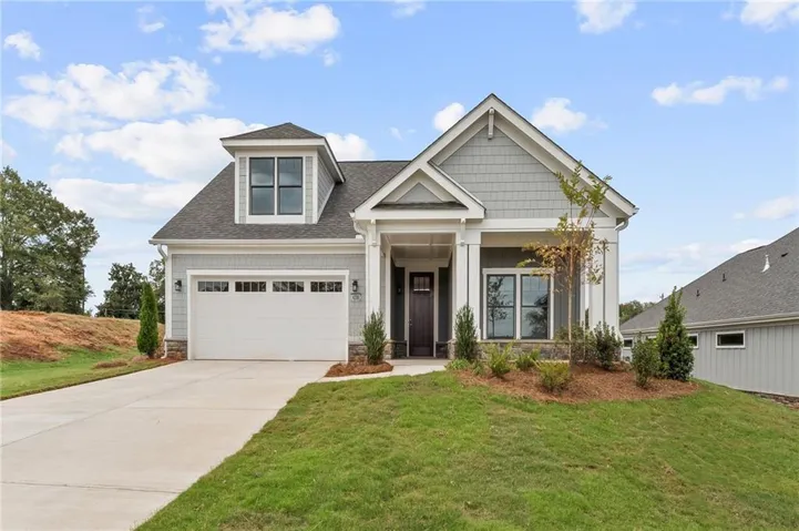 Craftsman house with roof with shingles, a front yard, driveway, and stone siding
