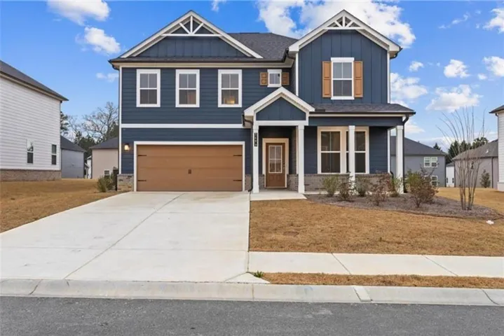 Two-story residence featuring a blue siding exterior with stone accents, a prominent two-car garage with a wood-finish door, and a covered front entry with white columns