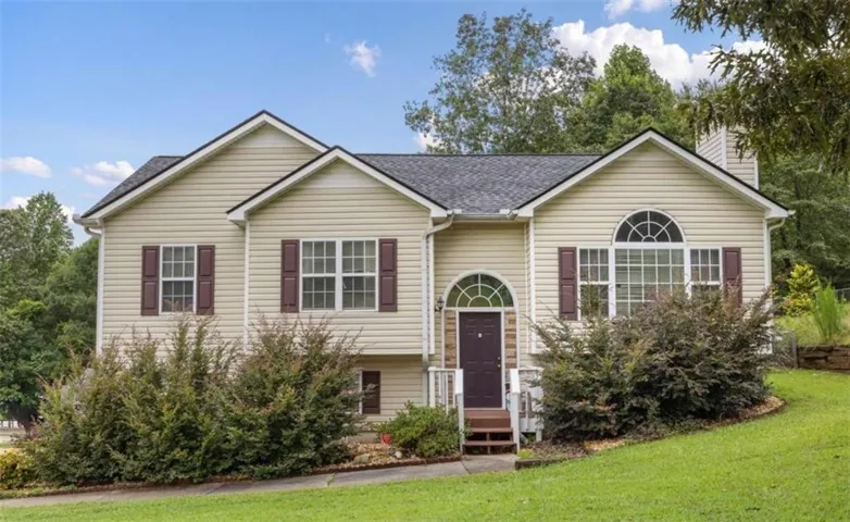 Exterior featuring light-colored siding, contrasting dark shutters, a prominent arched window, a gabled roofline, and established shrubbery