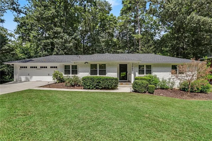 White brick exterior with a dark shingle roof, attached two-car garage, established front landscaping, and a concrete driveway