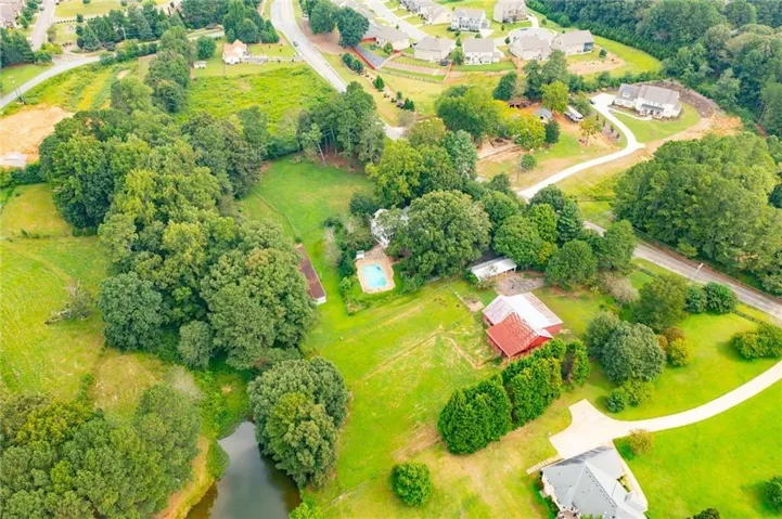 Expansive property featuring verdant green spaces, a private pond, mature trees, an outdoor swimming pool, and a red-roofed barn structure