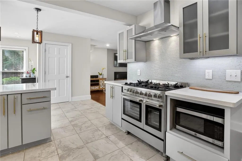 Kitchen with stainless steel appliances, glass fronted cabinets, gray cabinets, hanging light fixtures, and light marble finish floors
