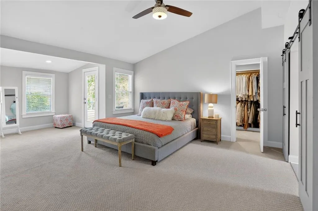 Bedroom with a barn door, lofted ceiling, light carpet, ceiling fan, and access to outside