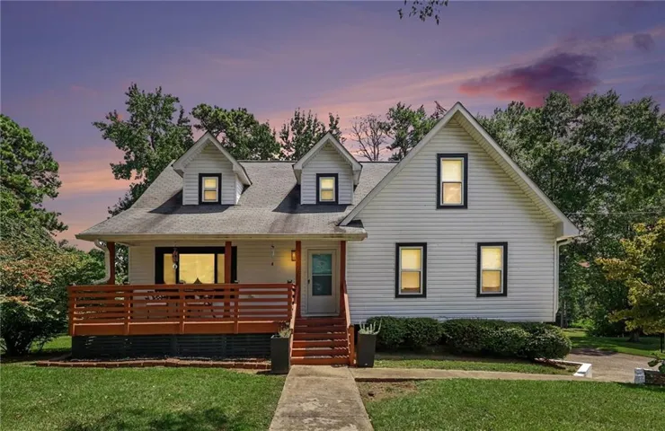 White siding exterior with black window trim, dormer windows, a wood deck with railings, and a concrete pathway