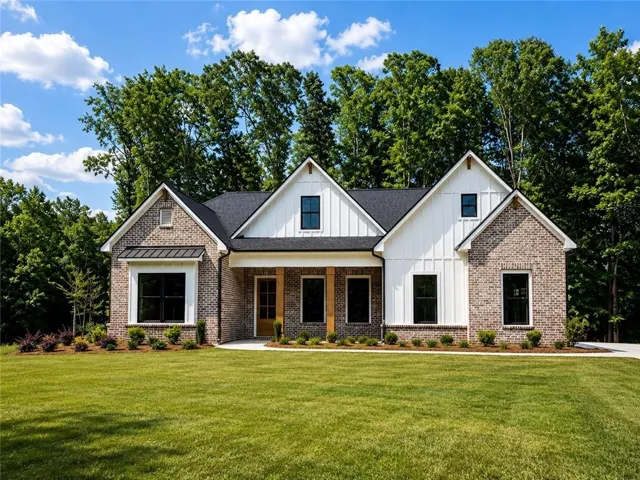 Modern farmhouse exterior featuring a brick facade with white board-and-batten accents, black-framed windows, a dark shingle roof, a covered front porch with exposed timber posts, and an expansive front lawn