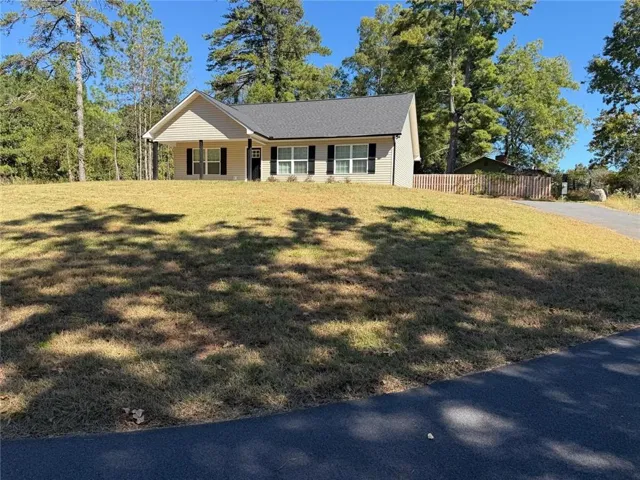 Single-story residence featuring light-colored siding, a dark shingle roof, black shutters, and a covered entry