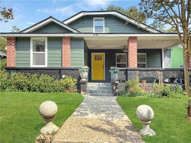 Front exterior with dark green siding, brick columns, a bright yellow front door, and a covered porch