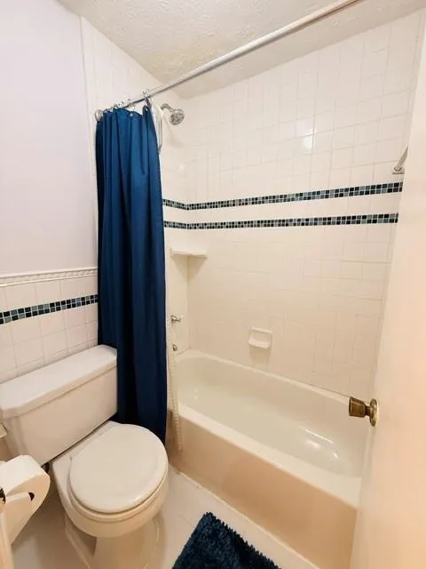 Full Bathroom featuring ceramic tile walls with decorative black tile accents, a combined tub and shower enclosure with chrome fixtures, and a ceramic toilet with elongated bowl