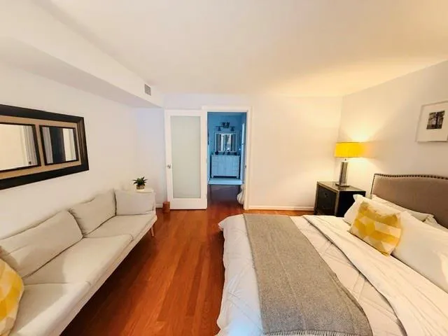 Spacious bedroom featuring warm wood-finish flooring, neutral wall finishes, and abundant natural lighting