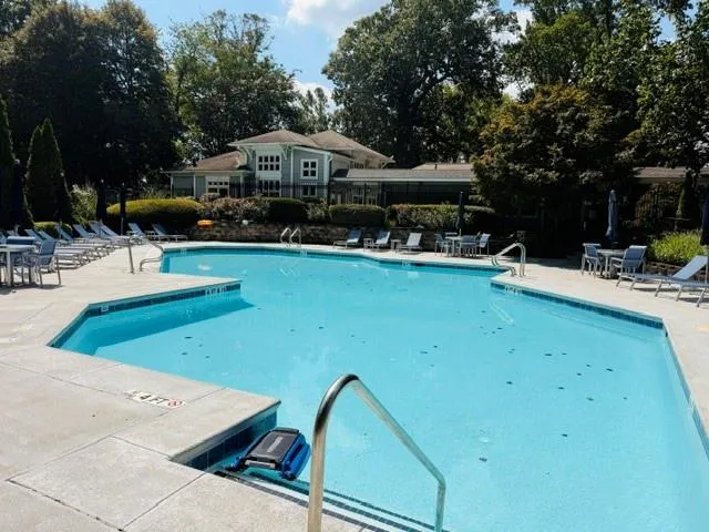 Resort-style community pool featuring crystal-clear water, spacious sun deck with lounge seating, shallow entry area, and mature landscaping surrounding the amenity