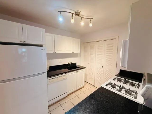 White cabinetry, black countertops, track lighting, white appliances, and tiled flooring