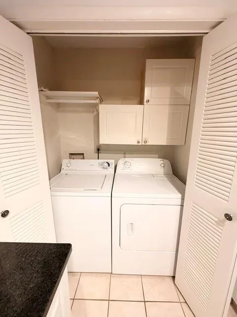 Dedicated laundry closet featuring side-by-side washer and dryer appliances, tile flooring, and upper cabinetry for storage