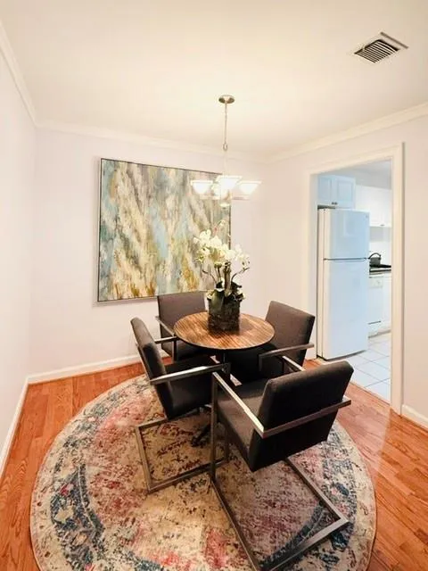 Elegant dining space featuring a round wood-top table, black upholstered chairs with metal frames, warm wood-finish flooring, and a patterned area rug