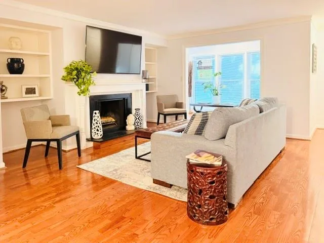Bright living room featuring hardwood flooring, a gas fireplace with built-in shelving, wall-mounted flat-screen television, and abundant natural light from sliding glass doors