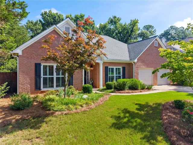Brick exterior featuring a two-car garage, shuttered windows, and a portico entry