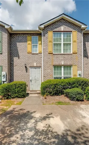 Brick exterior featuring a gabled roofline, decorative yellow window shutters, and a security screen door