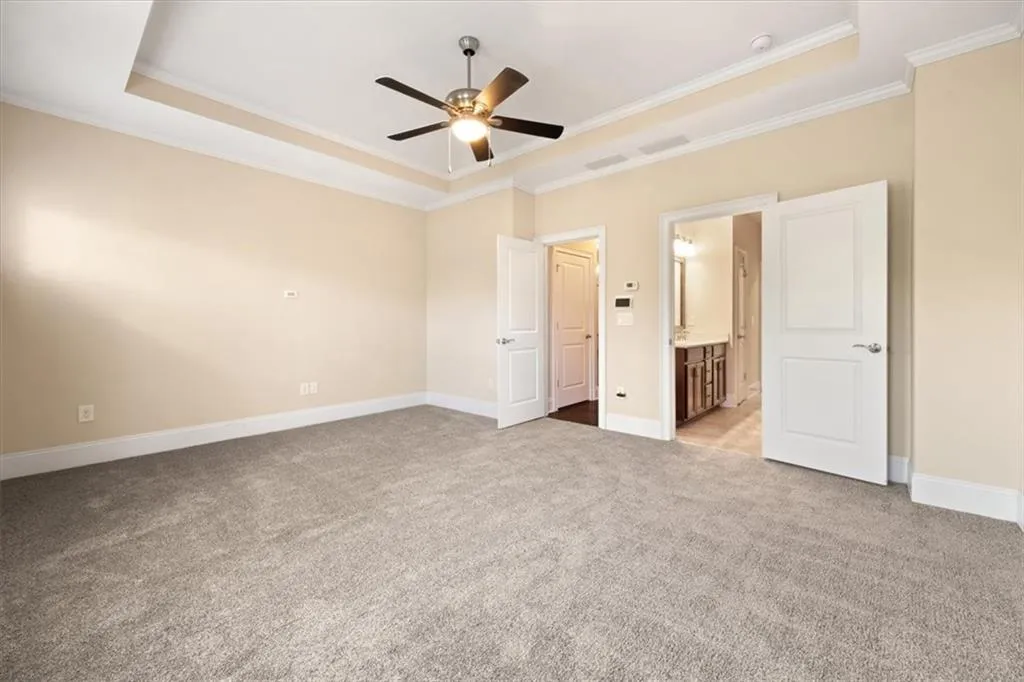 Unfurnished bedroom with light colored carpet, a raised ceiling, ceiling fan, and connected bathroom