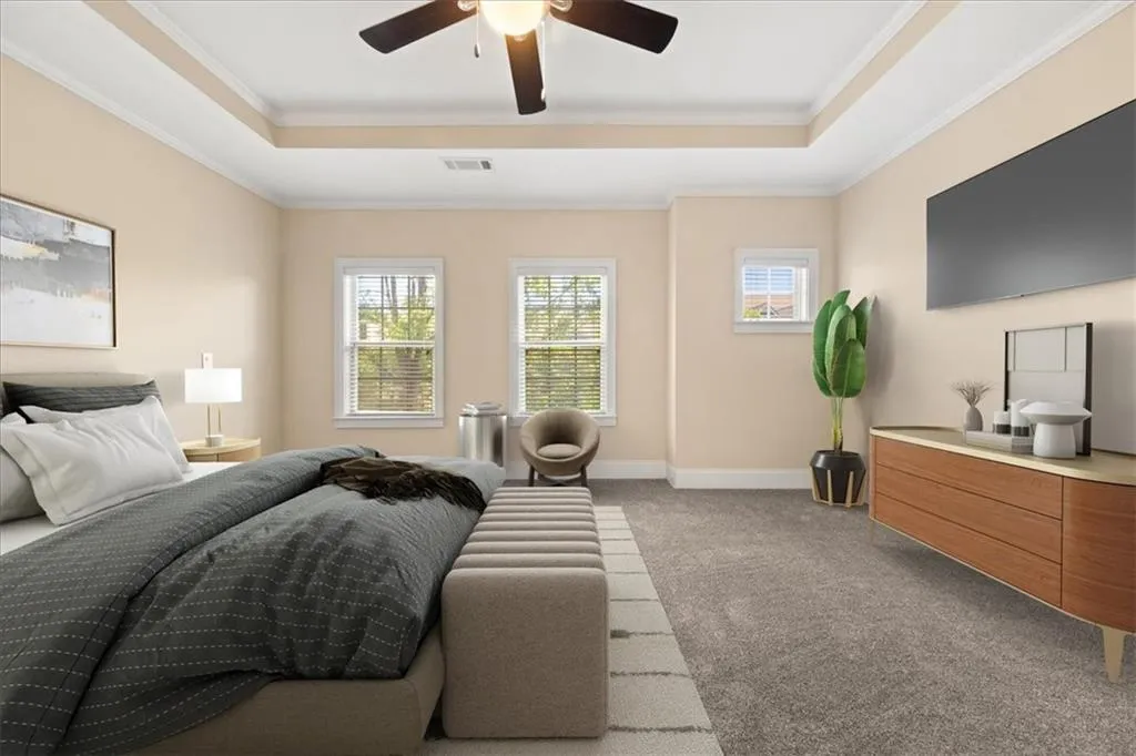 Carpeted bedroom with ceiling fan, a tray ceiling, and ornamental molding