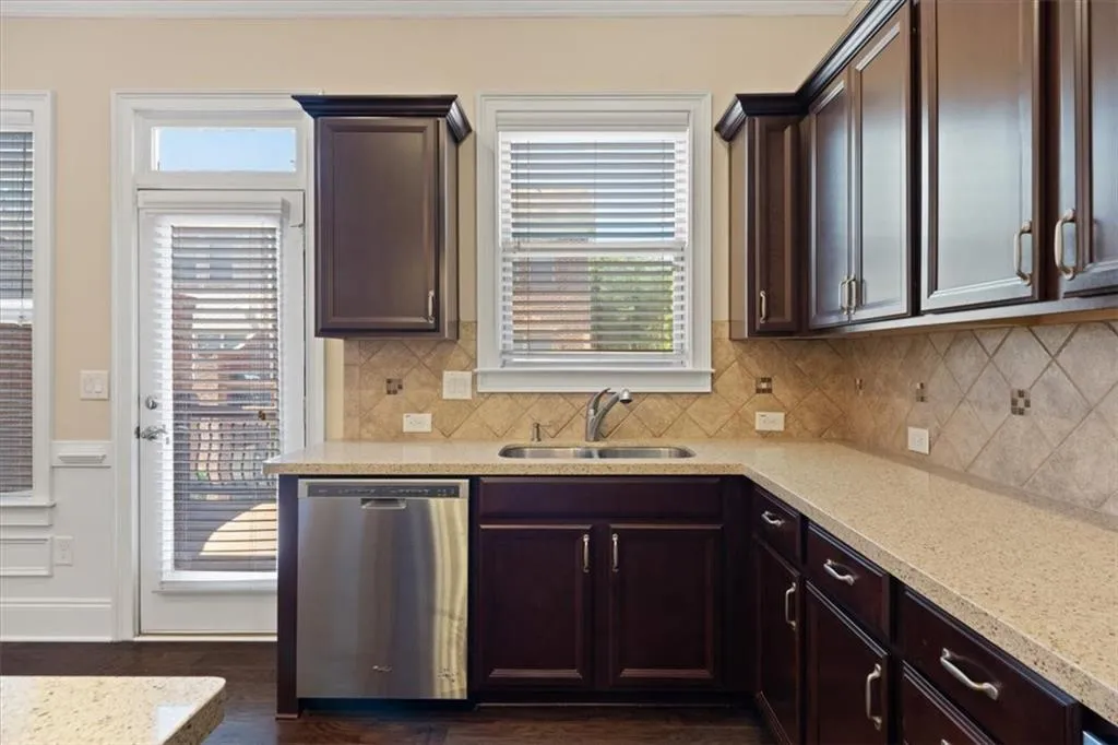 Kitchen with sink, tasteful backsplash, stainless steel dishwasher, dark hardwood / wood-style floors, and light stone countertops