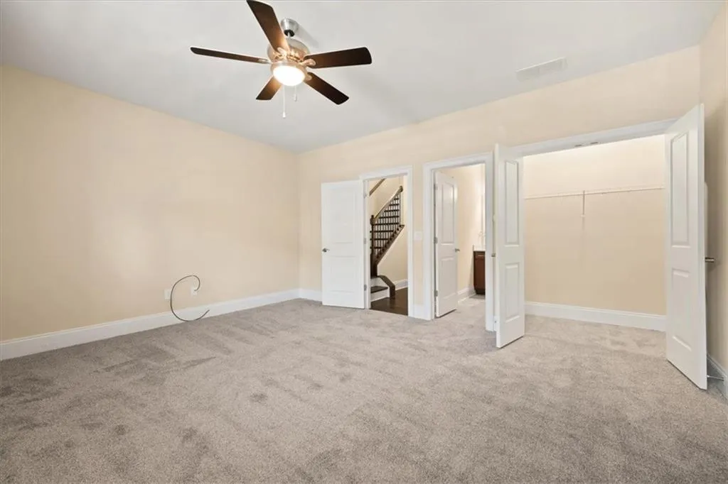 Unfurnished bedroom featuring a spacious closet, a closet, light carpet, and ceiling fan