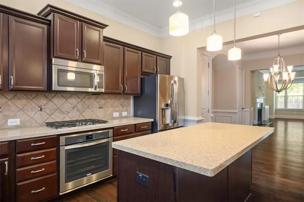 Kitchen featuring backsplash, stainless steel appliances, dark wood-type flooring, and hanging light fixtures