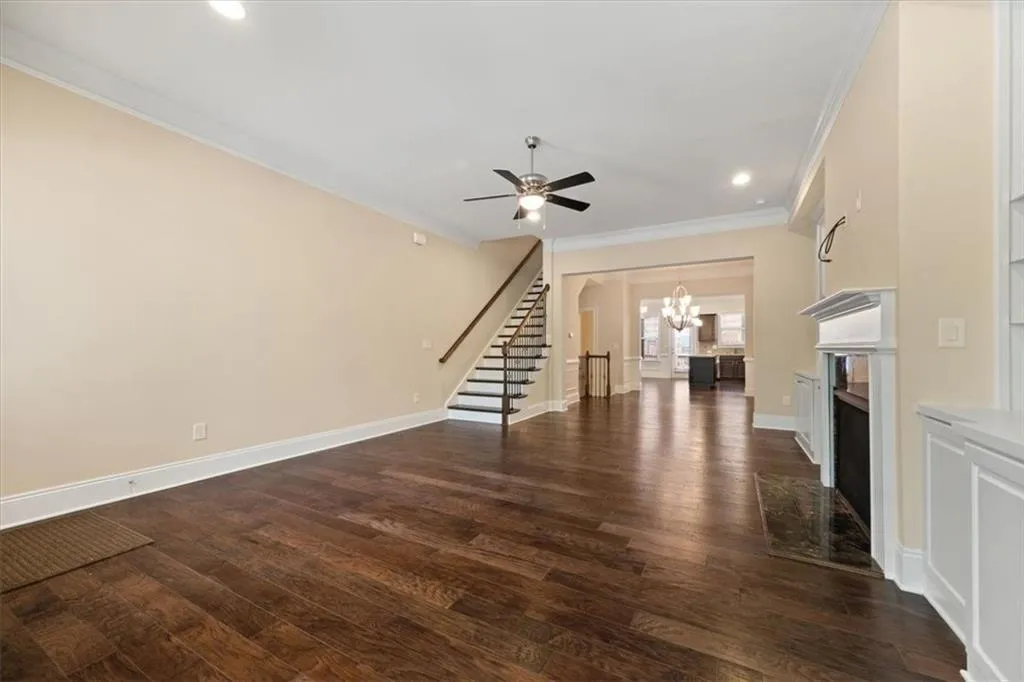Unfurnished living room featuring ceiling fan with notable chandelier, dark hardwood / wood-style floors, and crown molding