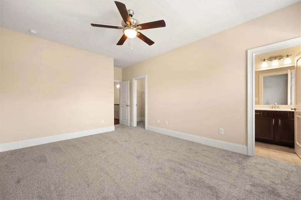 Unfurnished bedroom with ceiling fan, ensuite bathroom, light carpet, sink, and a spacious closet