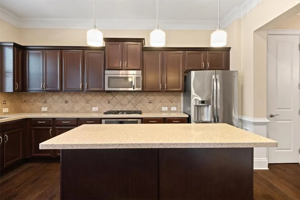 Kitchen with tasteful backsplash, decorative light fixtures, dark brown cabinets, stainless steel appliances, and dark hardwood / wood-style floors