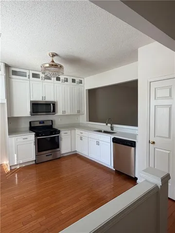 Kitchen featuring wood-finish flooring, white cabinetry, a pass-through window, and stainless steel appliances