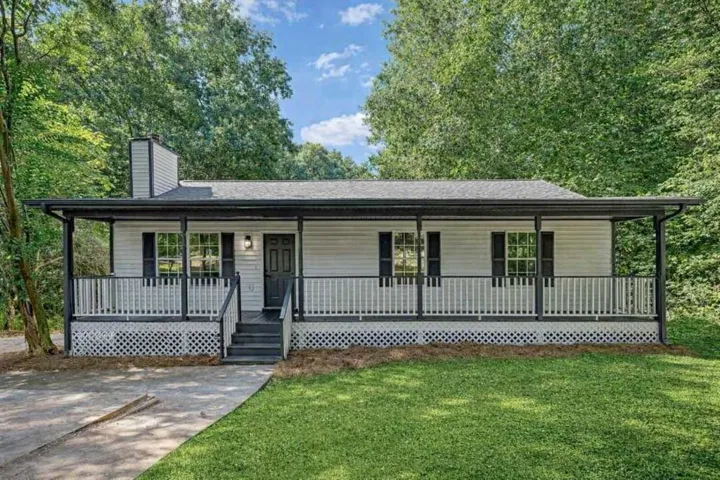 White siding exterior with a dark-trimmed covered porch, featuring a dark front door, white railing, and dark shutters