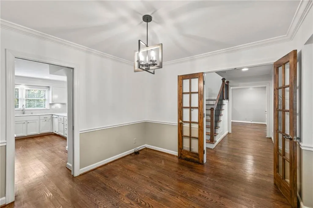 Unfurnished dining area featuring dark wood-type flooring, crown molding, french doors, and a chandelier