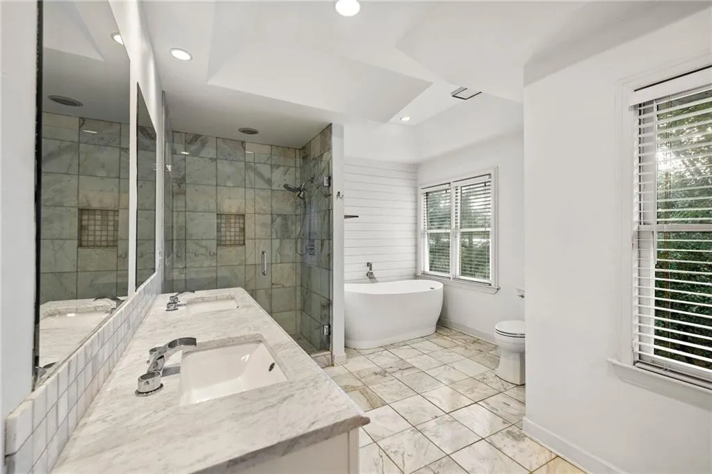 Full bath featuring a freestanding bath, double vanity, a shower stall, recessed lighting, and light marble finish flooring