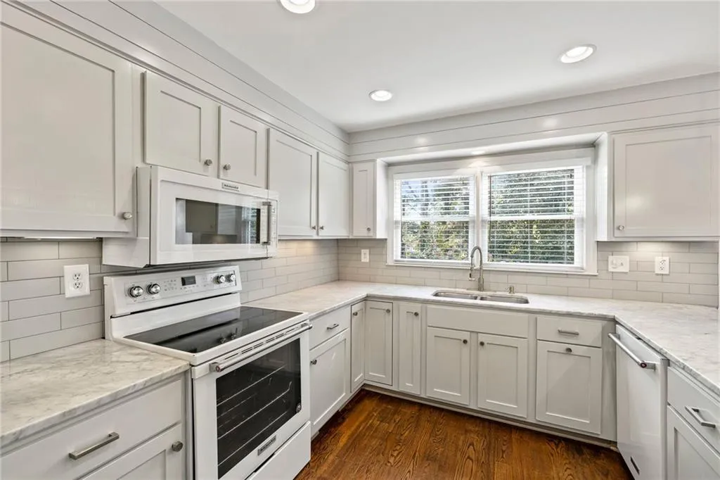 Kitchen with white appliances, white cabinetry, dark wood-type flooring, light stone countertops, and recessed lighting
