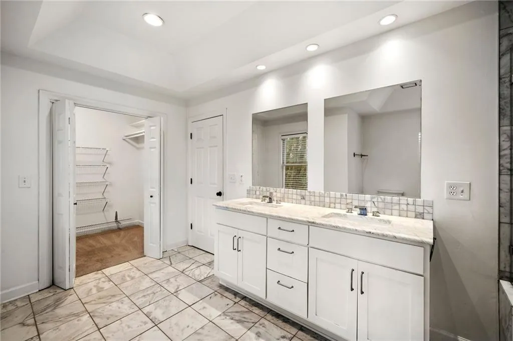 Bathroom featuring double vanity, recessed lighting, a spacious closet, decorative backsplash, and light marble finish flooring