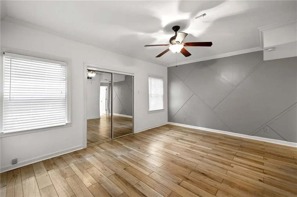 Unfurnished bedroom with ornamental molding, ceiling fan, light wood-type flooring, a closet, and a decorative wall