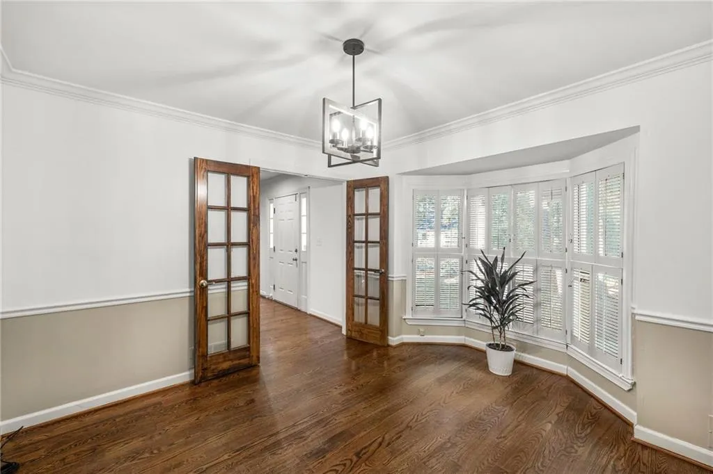 Unfurnished dining area featuring french doors, dark wood finished floors, crown molding, and a chandelier