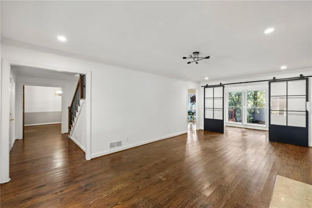 Unfurnished living room featuring a barn door, crown molding, dark wood-style floors, a chandelier, and recessed lighting