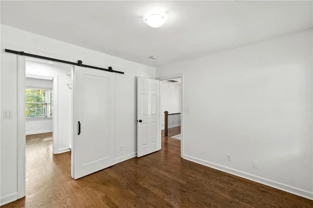 Unfurnished bedroom featuring a barn door and dark wood-style floors