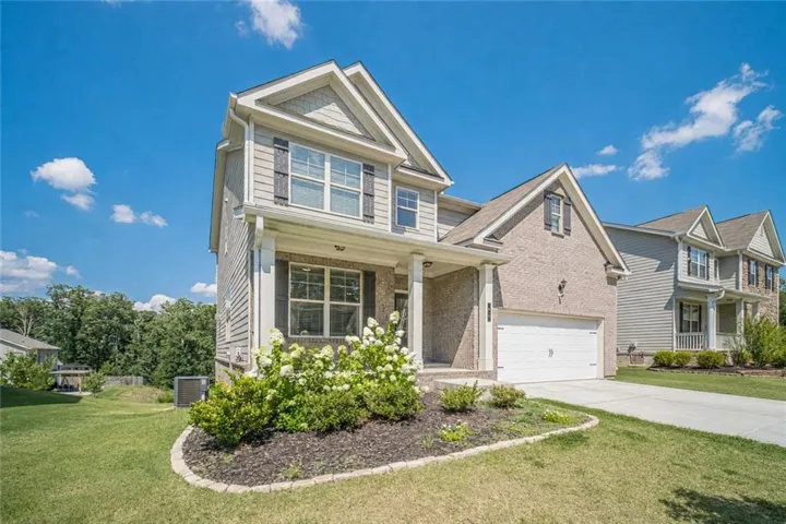 Two-story residence featuring a brick and siding exterior, an attached garage, and a covered porch entry