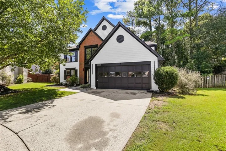 Modern exterior with white siding and dark trim accents, brick detailing, attached two-car garage, and mature trees