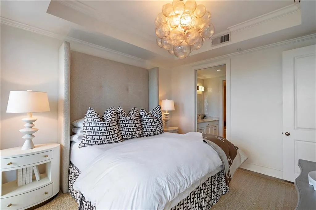 Recessed tray ceiling with crown molding, chandelier, upholstered headboard, carpeted flooring, and a mirrored closet door