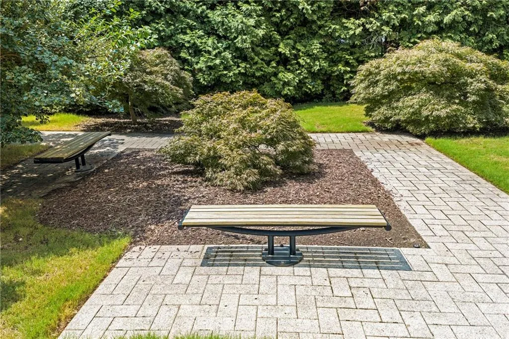 Landscaped grounds featuring patterned paver pathways, established trees, and two wooden benches