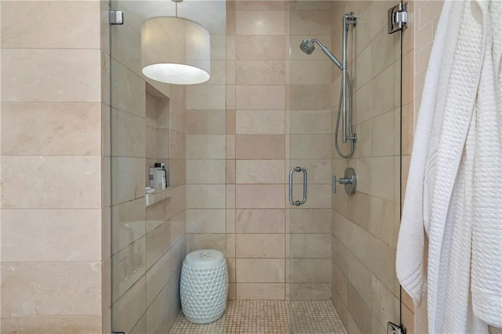 Glass-enclosed shower featuring large format wall tiles, a built-in shower niche, a handheld shower fixture, and mosaic tile flooring