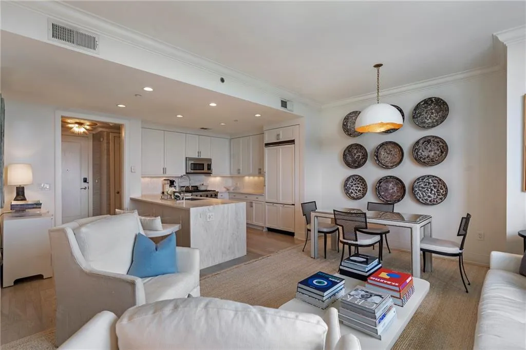 Open-concept living space featuring a kitchen with white cabinetry and stainless steel appliances, a kitchen island with stone countertop, and wood-finish flooring