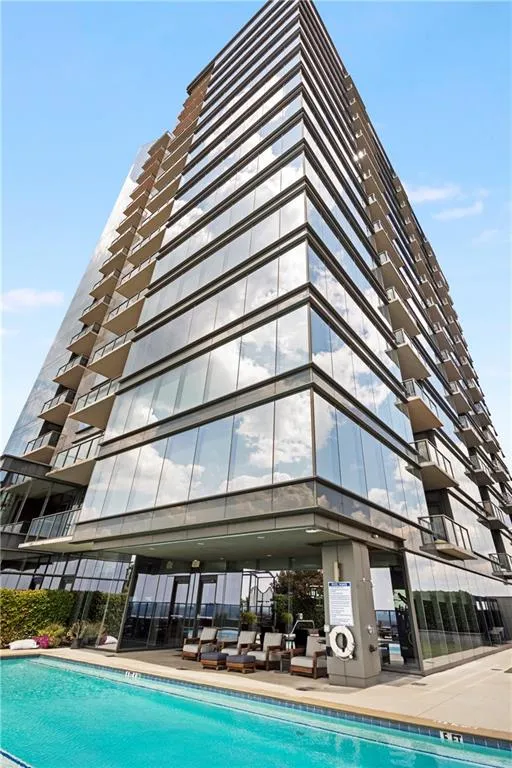 Modern high-rise building with a glass facade, multiple private balconies, and an outdoor swimming pool