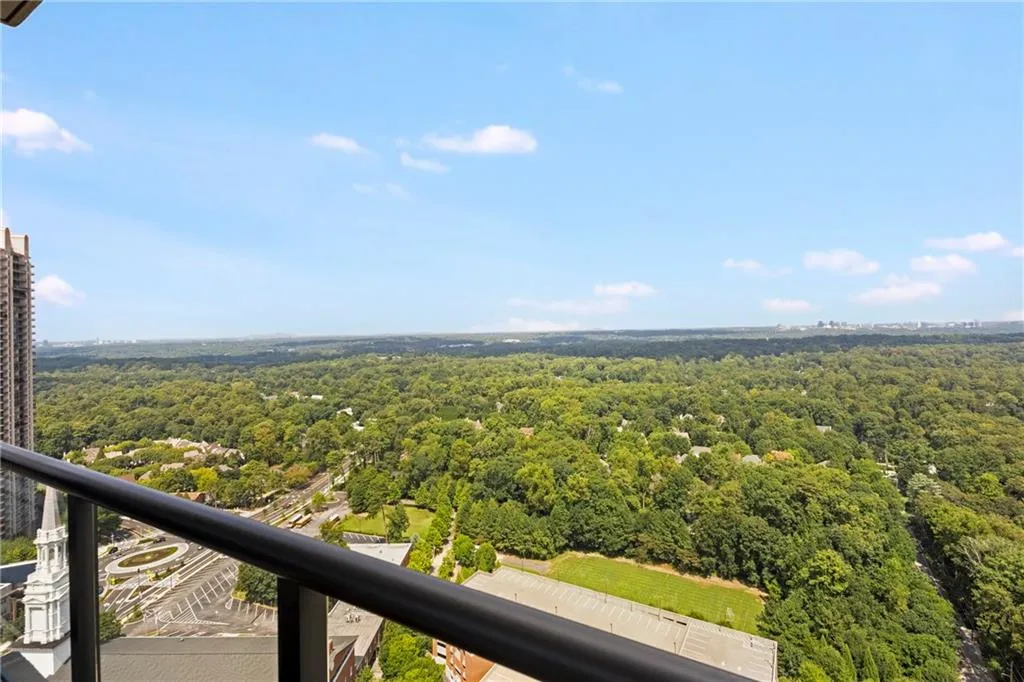 Expansive treeline vista from a high-level balcony featuring a black metal railing and transparent panels