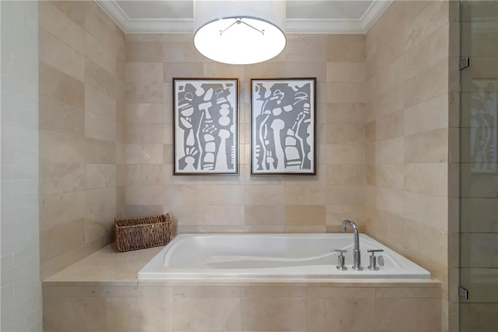 Built-in soaking tub with deck-mounted chrome fixtures, surrounded by light-toned tiled walls and a coordinating tiled tub deck
