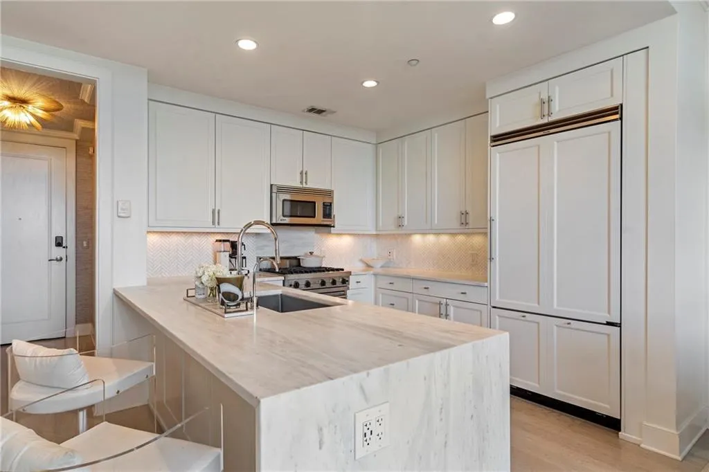 Kitchen featuring white shaker cabinetry, an integrated refrigerator, stainless steel appliances, a tiled backsplash, and a large island with a surface-mounted sink